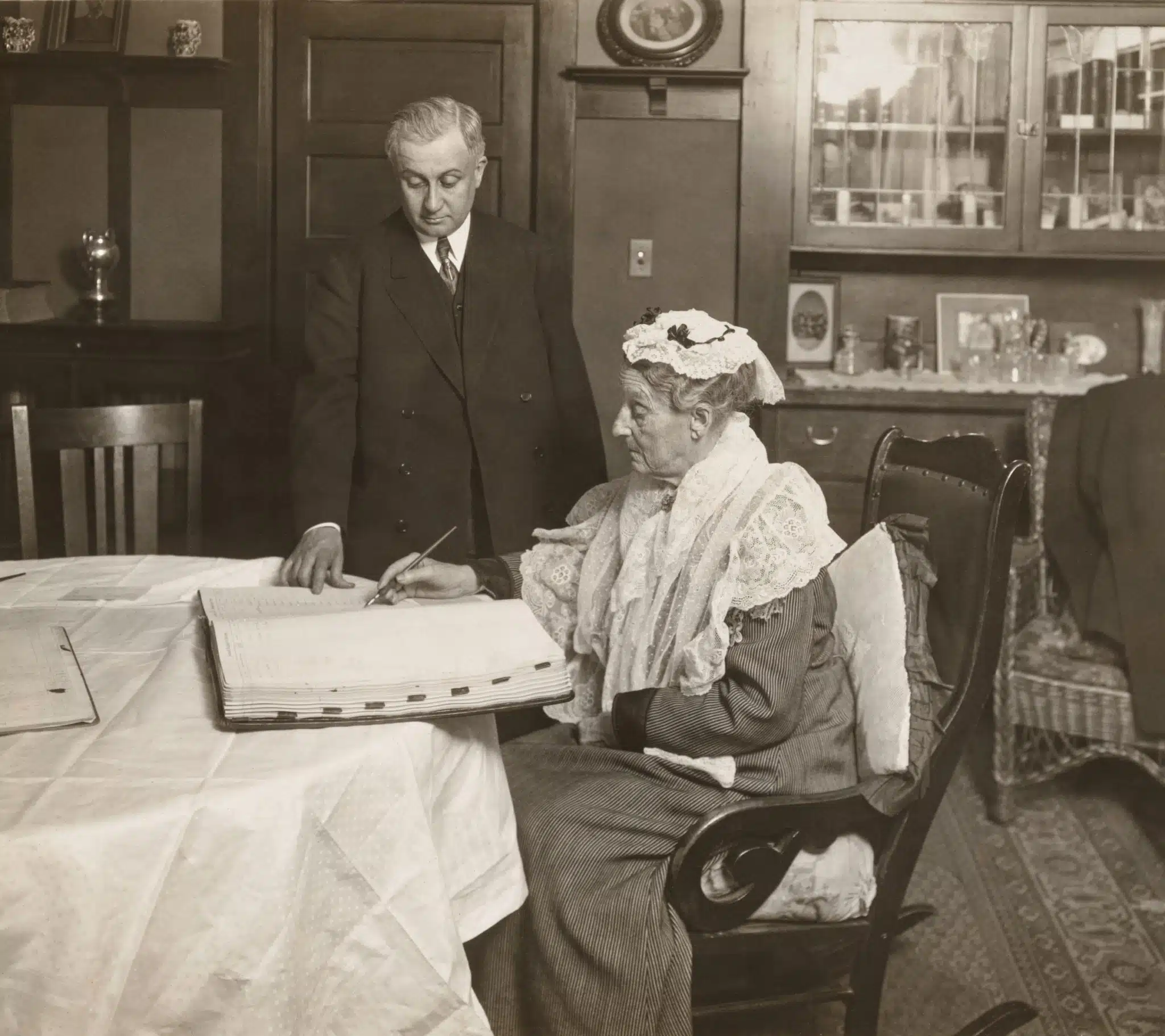 Abigail Scott Duniway seated signing a voter registration book, with County Clerk John B. Coffey standing beside her.