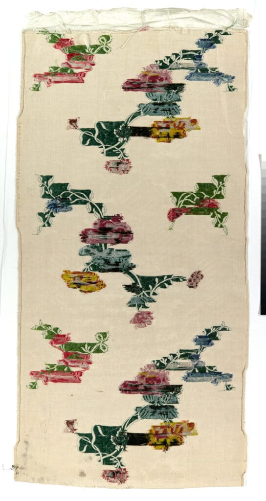 A narrow silk textile panel with multicolored floral motifs on a pale background.
