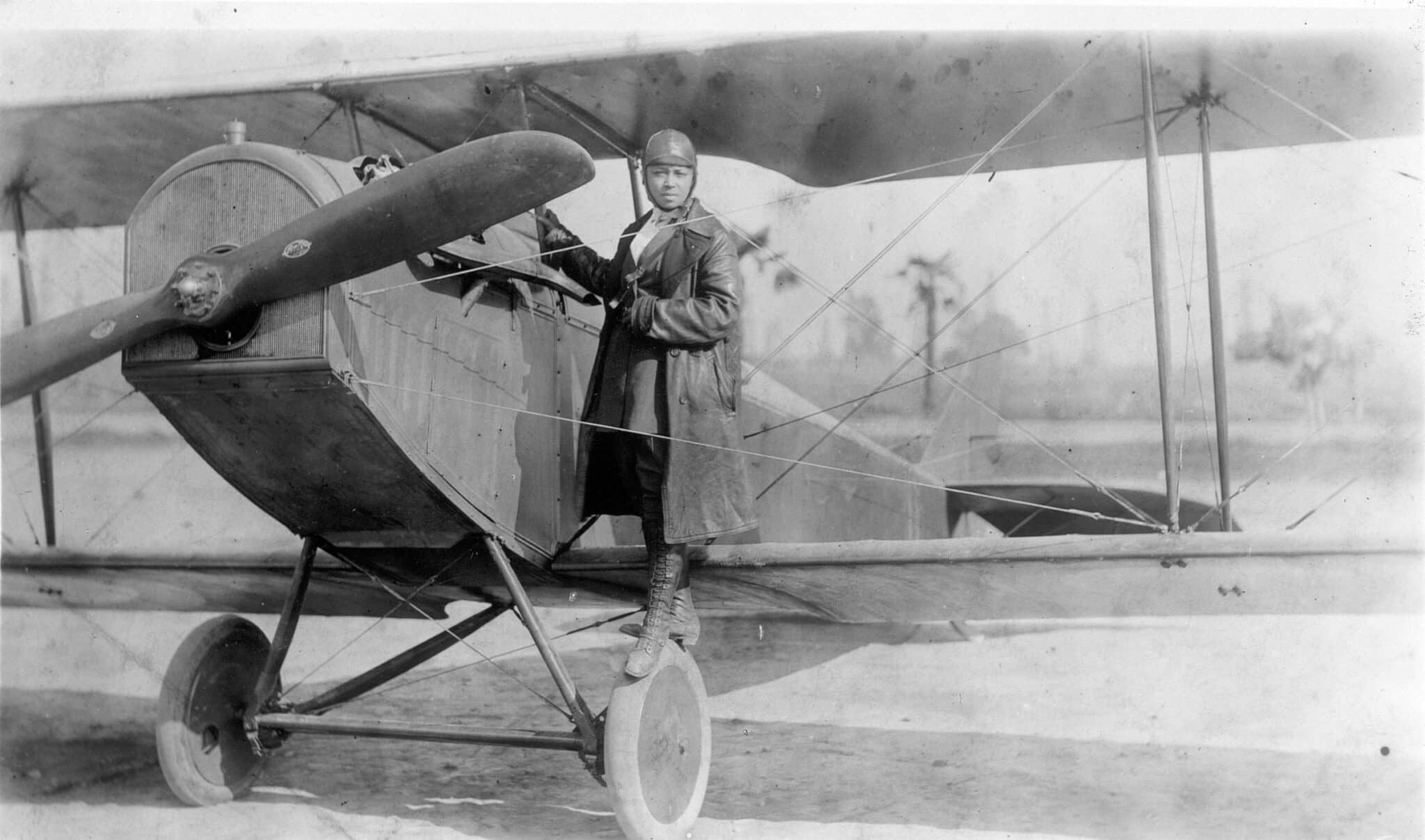 Bessie Coleman standing beside the cockpit of a biplane.