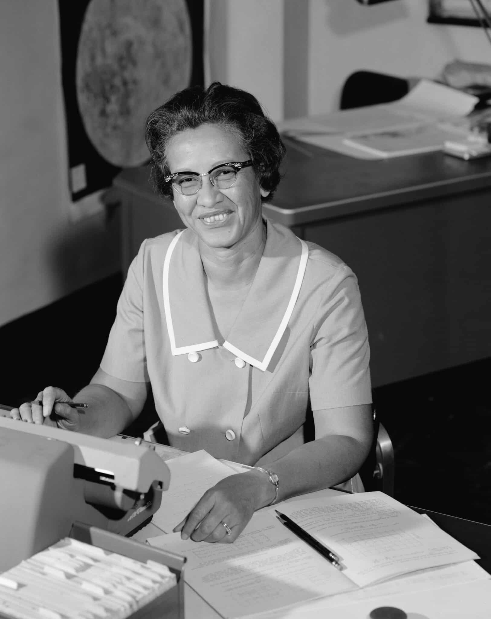 Katherine Johnson seated at a desk with papers and a calculating machine.