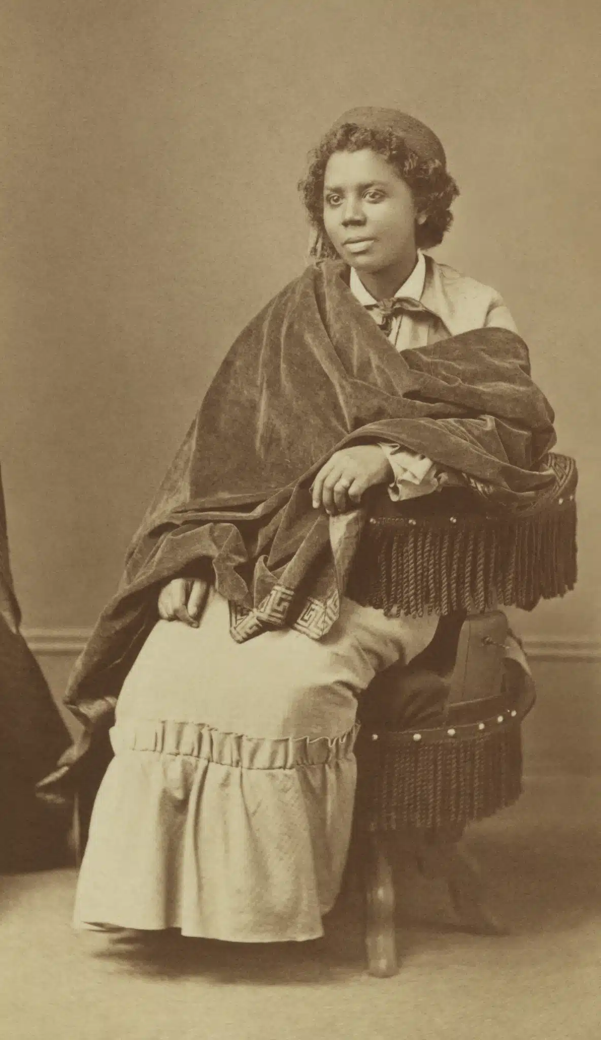 Edmonia Lewis seated, with one arm resting on a chair.