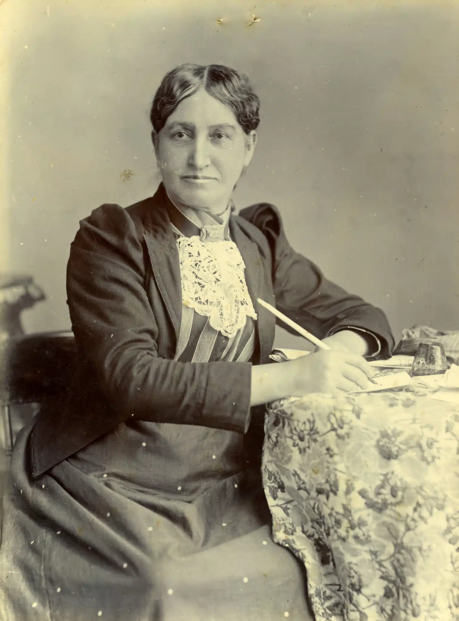 Elizabeth Yates seated beside a table with a floral covering.