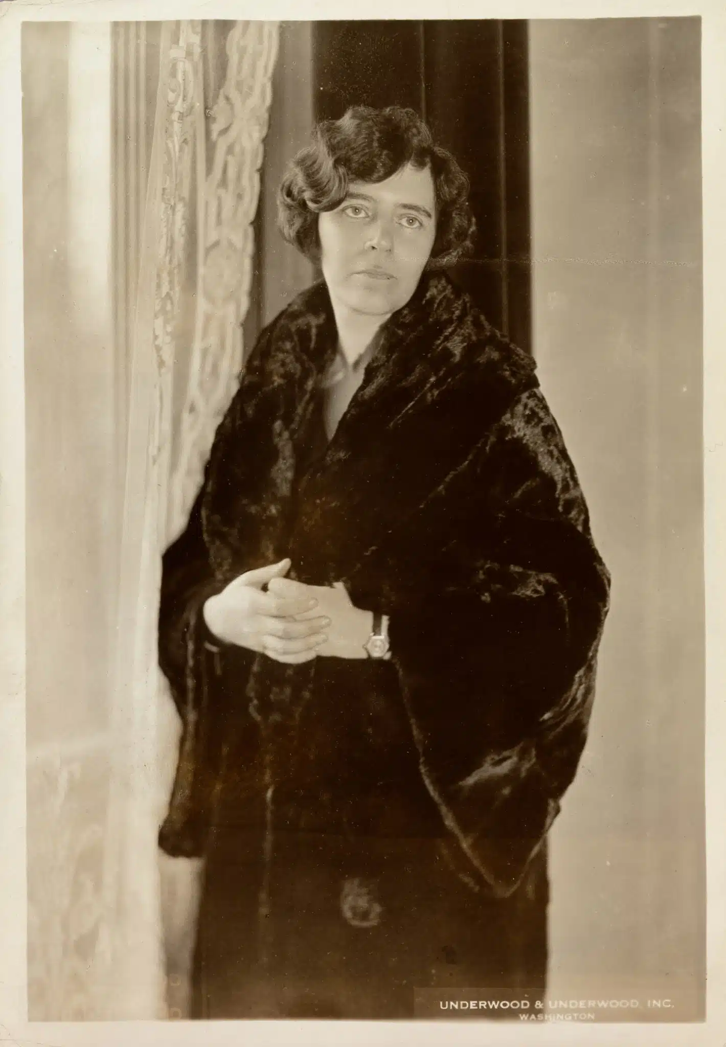 Alice Paul standing beside a curtain in a dark coat.