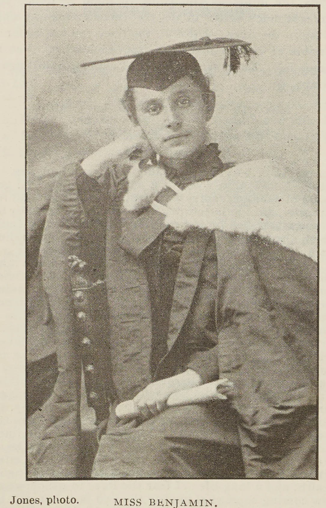 Ethel Benjamin seated in an academic cap and gown, holding an open book beside a carved chair.
