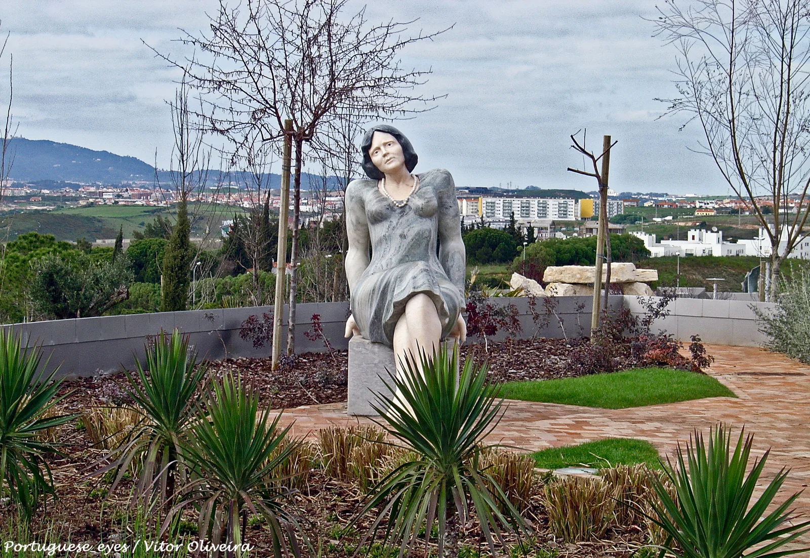 Florbela Espanca statue in Parque dos Poetas, 2015 | Amazing Women In History Francisco Simões’s seated statue of Florbela Espanca in Parque dos Poetas, with trees and buildings behind it.