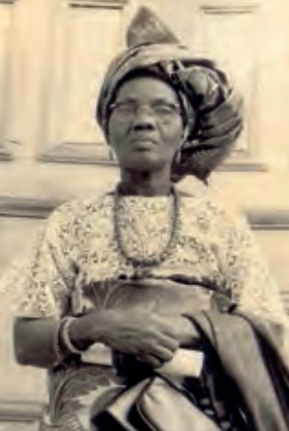 Funmilayo Ransome-Kuti at seventy in 1970 | Amazing Women In History Funmilayo Ransome-Kuti wearing glasses, a headwrap and patterned dress, holding a handbag in front of her.