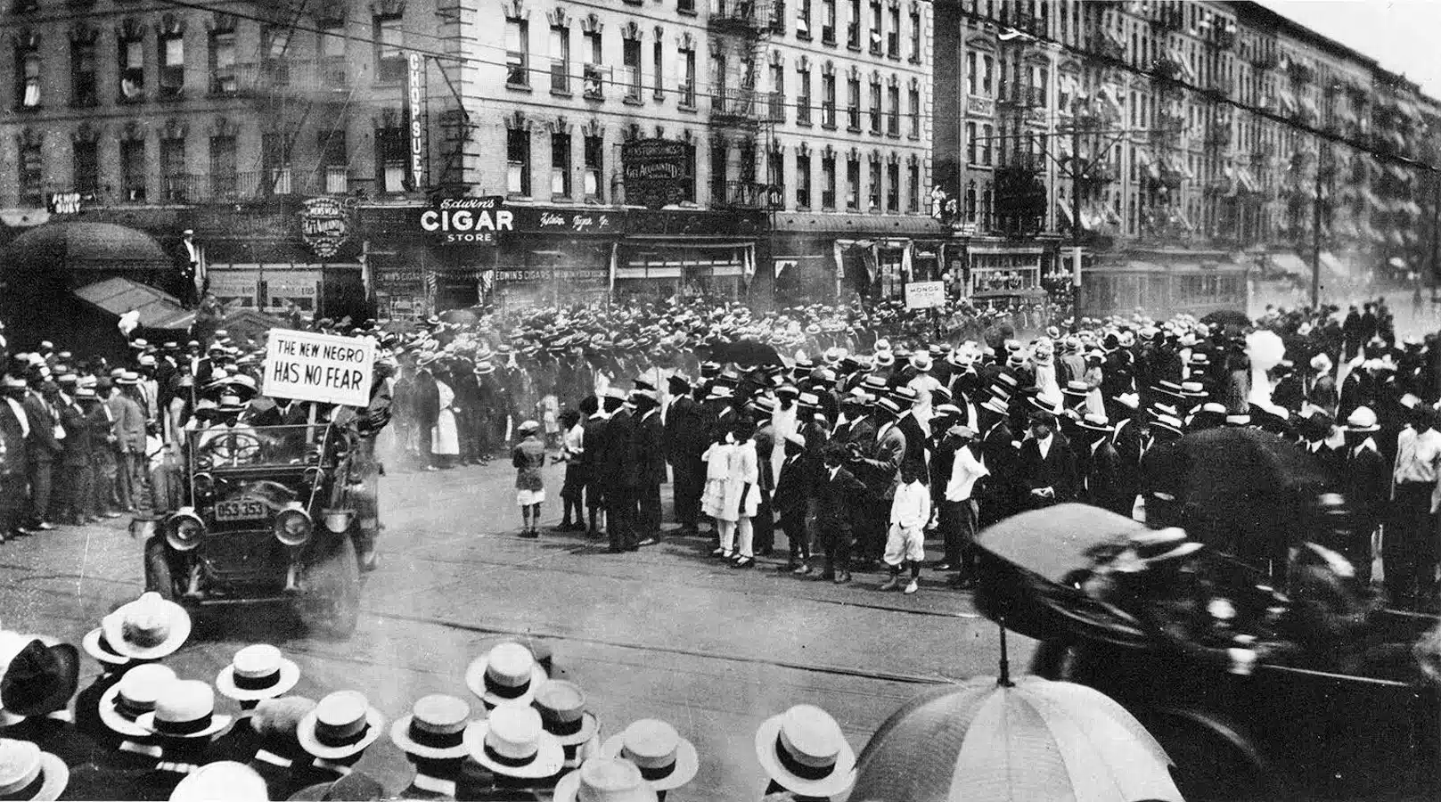 A UNIA parade passes crowds and buildings in Harlem.