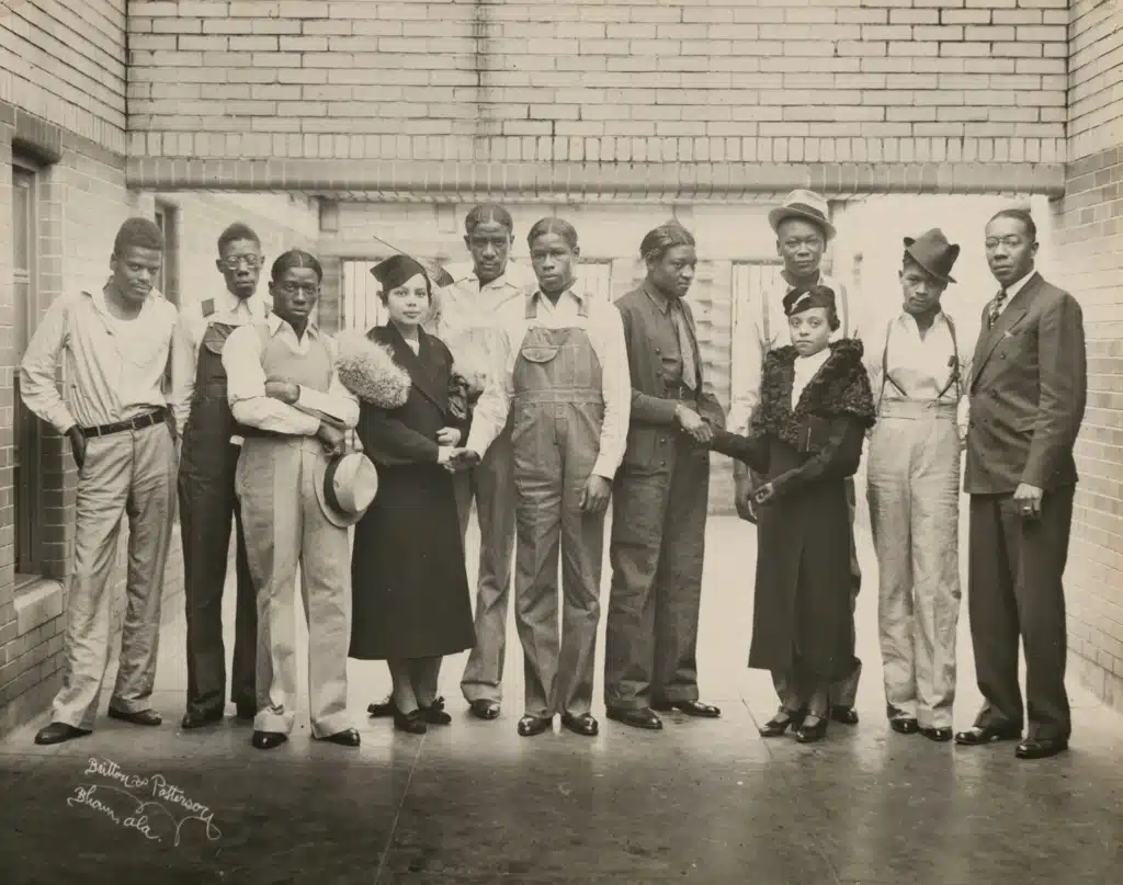 Juanita Jackson Mitchell and the Scottsboro Boys pose together outside a brick building.
