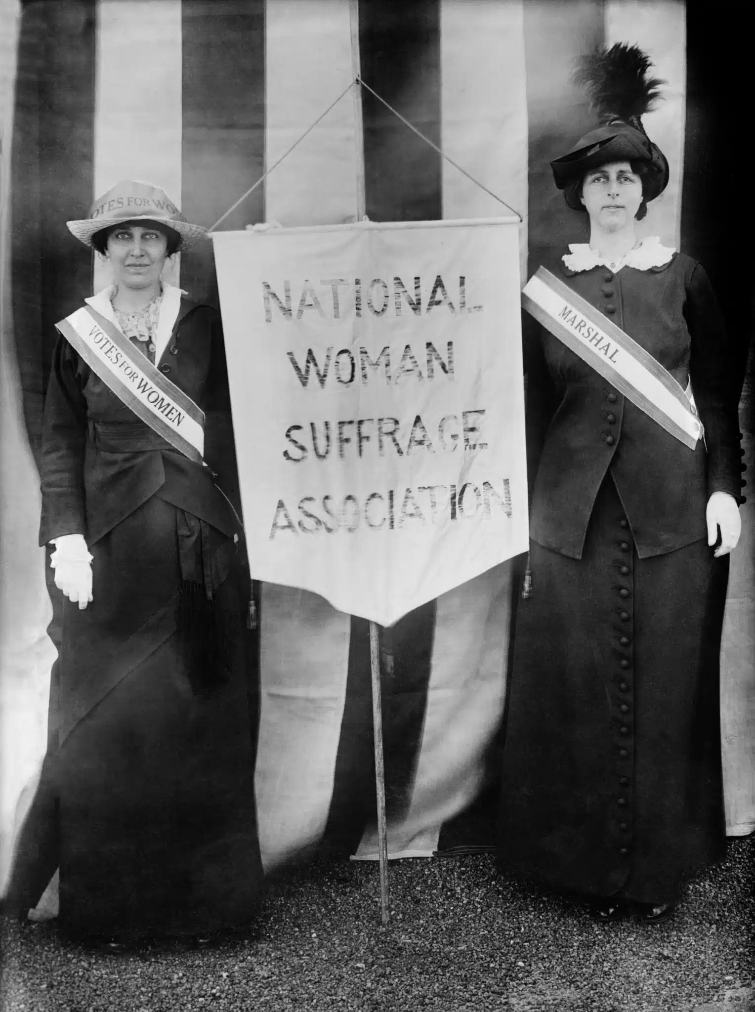 Two suffragists hold a National Woman Suffrage Association banner.