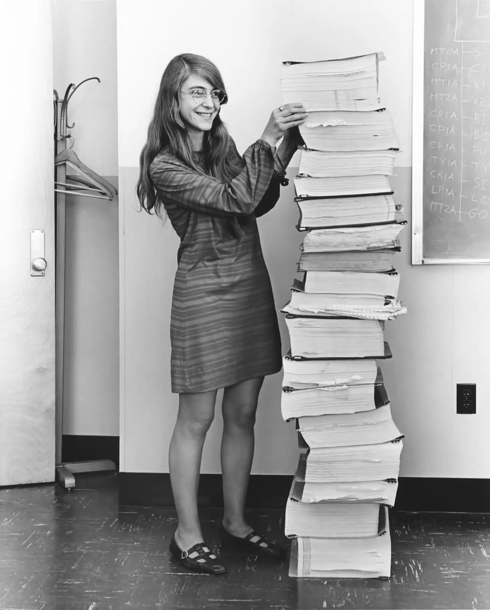 Margaret Hamilton stands beside a tall stack of Apollo software listings.