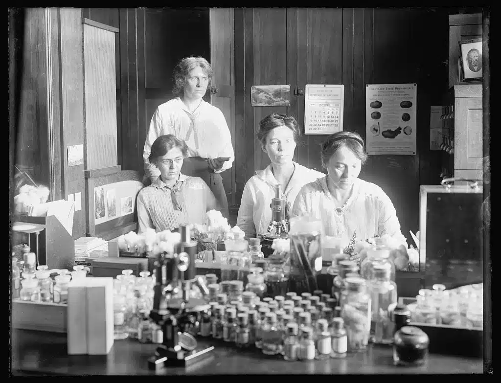 Four women scientists work among laboratory glassware and equipment.