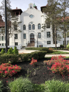 College Hall at Montclair State University, 2021 | Amazing Women In History College Hall’s white facade and bell tower at Montclair State University, beyond a flower garden.
