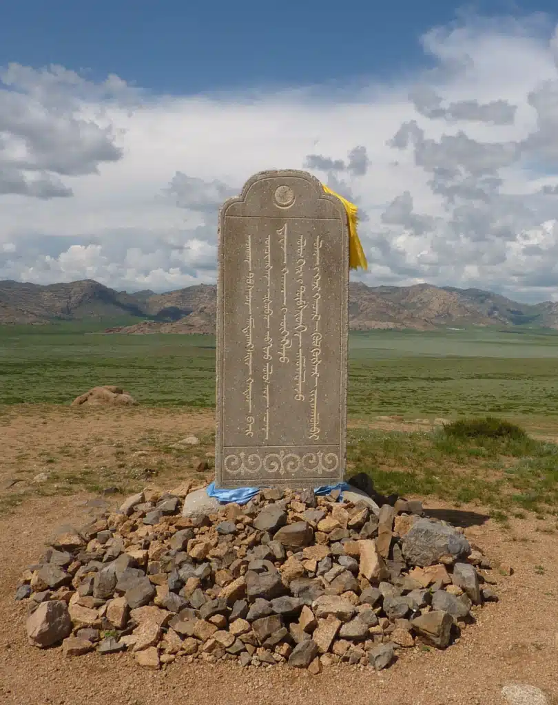 Inscribed memorial stone for Mandukhai Khatun on a pile of rocks in a grassy Mongolian landscape.