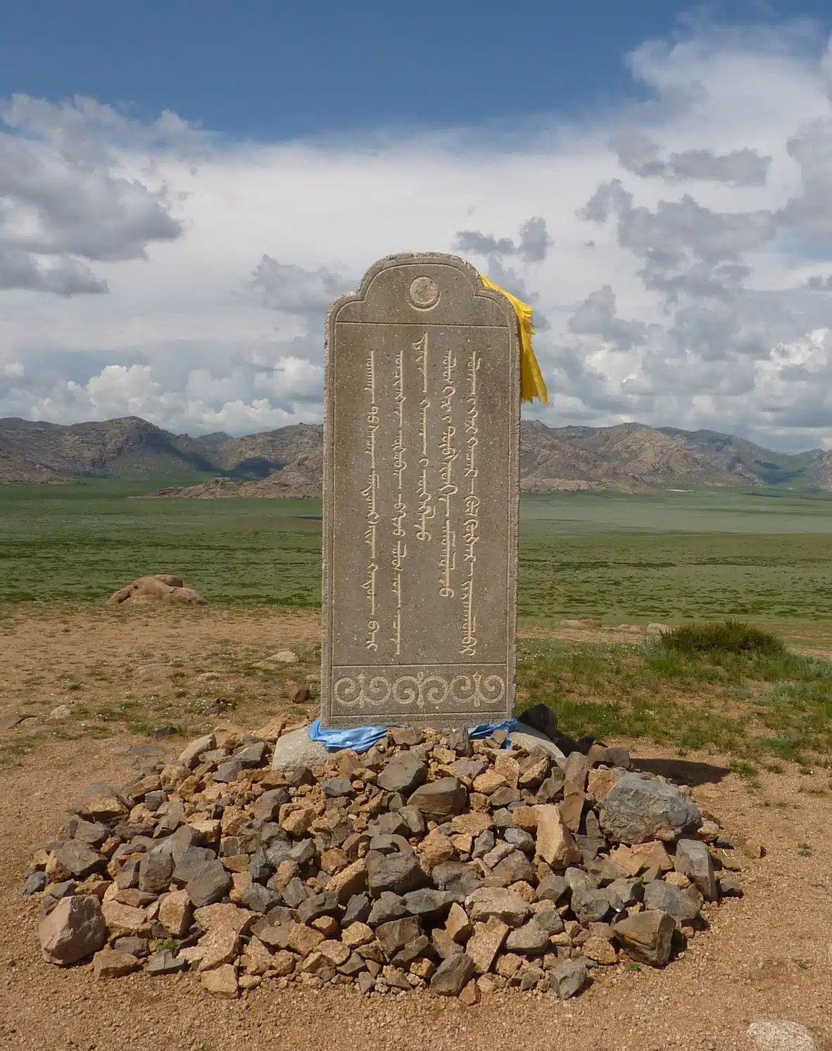 Inscribed memorial stone for Mandukhai Khatun on a pile of rocks in a grassy Mongolian landscape.