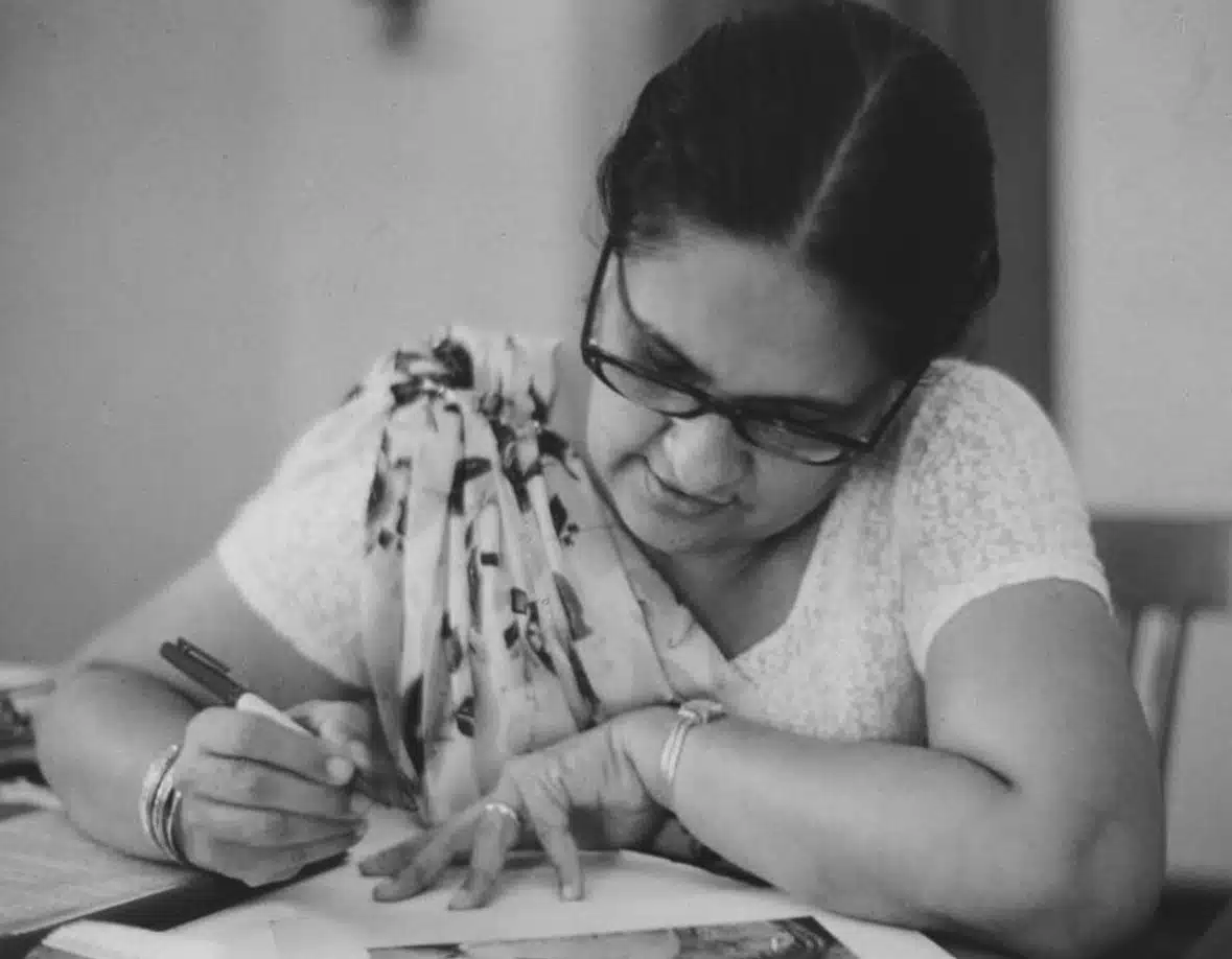 Sirimavo Bandaranaike writes at a desk, wearing glasses and a sari.